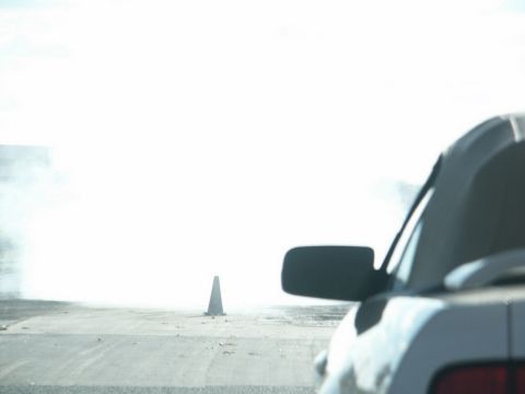 2001 Mercury Grand Marquis - A car is seen from the side, creating a large cloud of smoke during a burnout with a traffic cone in the background.