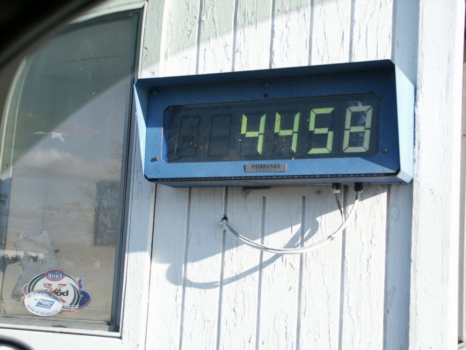Digital scale display showing 4458, mounted on a white wooden wall next to a window with NHRA stickers