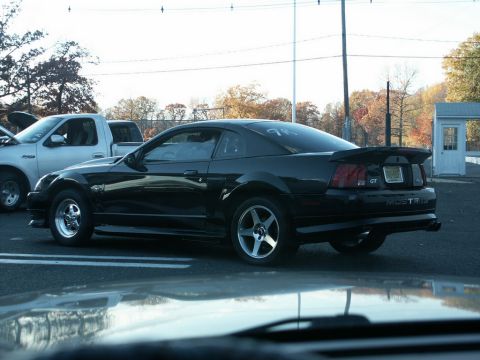2001 Mercury Grand Marquis - Black Ford Mustang GT seen from the rear, parked next to a white pickup truck.