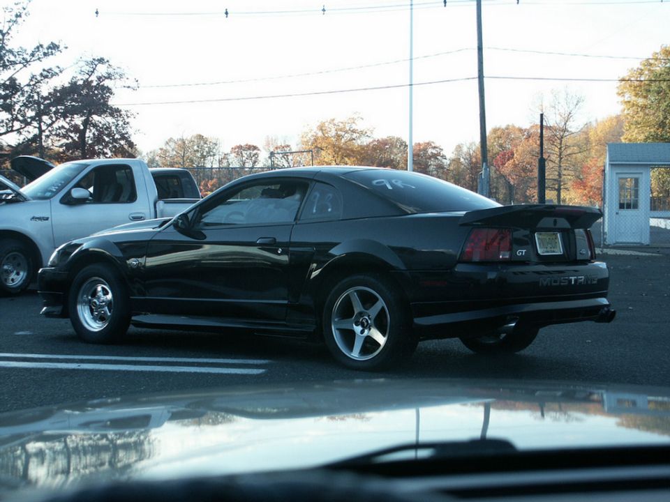 Black Ford Mustang GT with a spoiler and racing wheels parked next to a white pickup truck