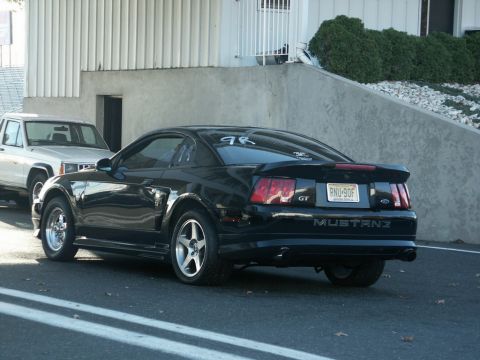 2001 Mercury Grand Marquis - A black Ford Mustang GT is parked next to a white Jeep Cherokee, with a building in the background.