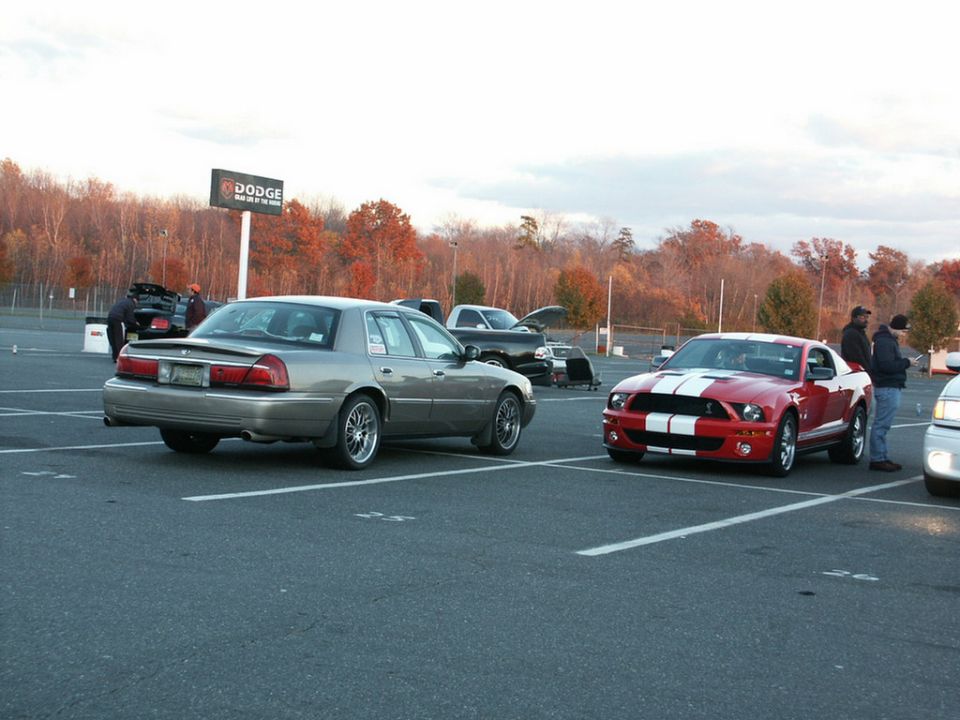 Gray sedan parked in a lot, rear view. Visible side trim and aftermarket wheels