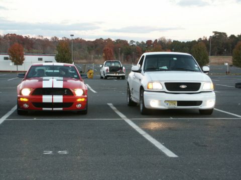 2001 Mercury Grand Marquis - Two vehicles, a red Mustang and a white pickup truck, are parked in an outdoor lot under a cloudy sky.
