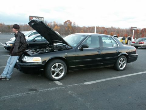 2001 Mercury Grand Marquis - A person leans on the front fender of a black 2001 Mercury Grand Marquis with its hood up.