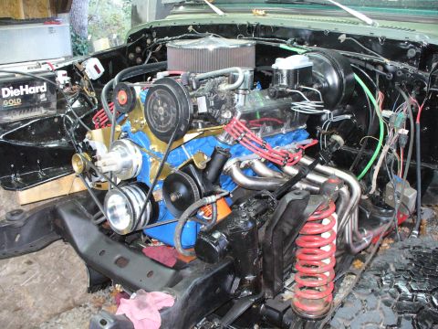 1978 Ford Bronco - Engine bay of a stripped 4x4 project with the fenders off, showing a blue-painted V8 with chrome valve covers, gold timing cover, chrome ro…
