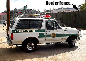 1994 Ford Bronco - A white Border Patrol SUV with a light bar and push bar is parked near a border fence.