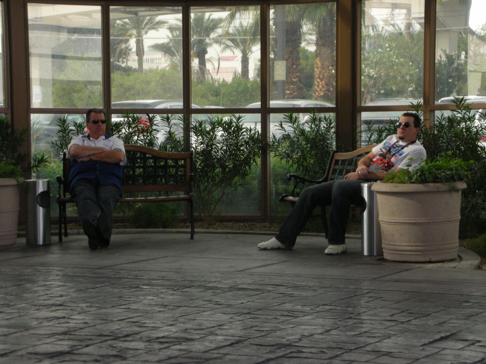Two men sitting on benches in a glass-walled atrium with potted plants