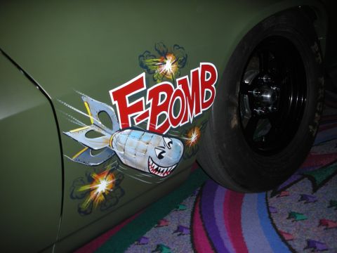 1998 Ford Crown Victoria - close-up shows a red F-Bomb logo and grinning cartoon bomb airbrushed on the matte green fender beside a black wheel.