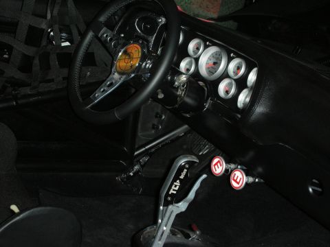 1998 Ford Crown Victoria - stripped race-car interior shows a roll cage, a black steering wheel, Autometer gauges, and a ratchet shifter on the console.