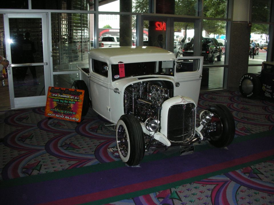 White chopped hot rod pickup with exposed engine displayed indoors on carpet