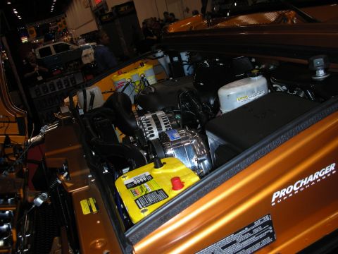 1998 Ford Crown Victoria - engine bay of an orange custom vehicle showing a chrome alternator, yellow battery and a ProCharger supercharger badge.