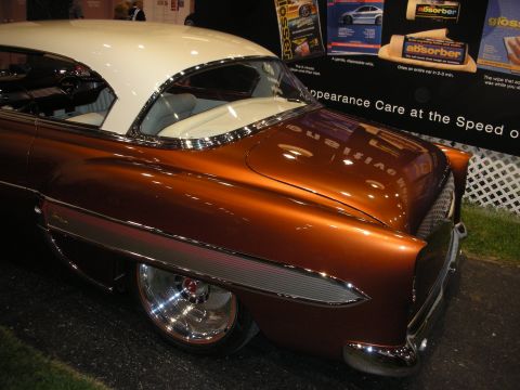 1998 Ford Crown Victoria - rear quarter of a copper-brown custom 1950s car with a white roof, chrome fender trim and polished wheels at an indoor show.