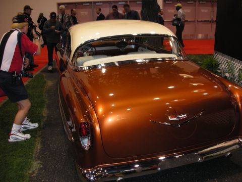 1998 Ford Crown Victoria - photographer crouches to shoot the chrome rear of a copper-brown custom car with a white roof on an indoor show floor.