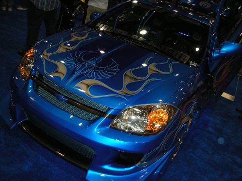 1998 Ford Crown Victoria - front of a custom blue Chevrolet coupe with silver tribal flames and an airbrushed bird across the hood, headlights lit.