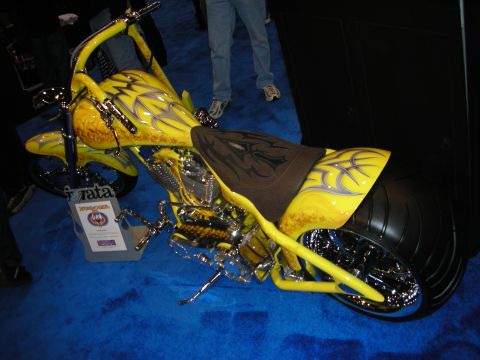 1998 Ford Crown Victoria - yellow custom chopper motorcycle with purple tribal graphics, chrome details and a fat rear tire displayed on blue carpet.