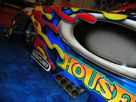 1998 Ford Crown Victoria - close-up of a brightly painted drag car body showing exhaust headers, a Freightliner decal and large outlined HOUSE lettering.