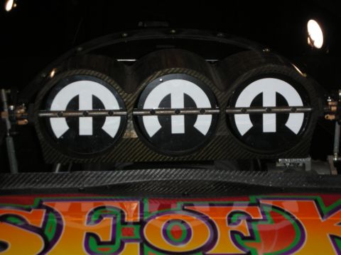 1998 Ford Crown Victoria - Three white Mopar 'M' logo discs mounted on a carbon-fiber panel above colorful outlined lettering, on a black background.