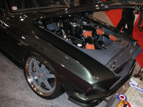 1998 Ford Crown Victoria - front quarter of a dark green custom Mustang fastback with an open hood revealing the engine and orange accents, lowered on staggered wheel…