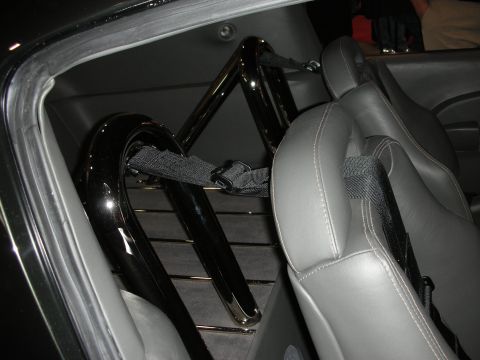 1998 Ford Crown Victoria - polished black roll bar mounted behind gray leather seats with harness straps inside a custom car interior.