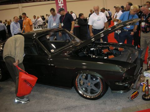 1998 Ford Crown Victoria - Show attendees gather around a dark green custom Mustang fastback with an open hood and staggered polished wheels.