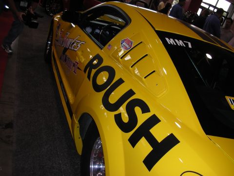 1998 Ford Crown Victoria - yellow custom Mustang race car with large black ROUSH lettering, hood louvers and an MM7 marking on the rear glass.