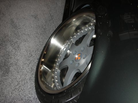 1998 Ford Crown Victoria - Detail of a polished split-rim alloy wheel with an orange-and-black logo center cap mounted on a dark vehicle.