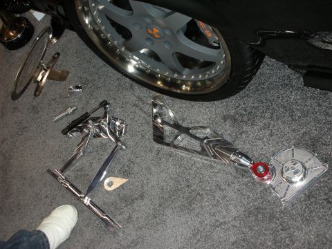 1998 Ford Crown Victoria - Chromed suspension control arms and steering linkage parts displayed on the floor next to a polished alloy wheel.