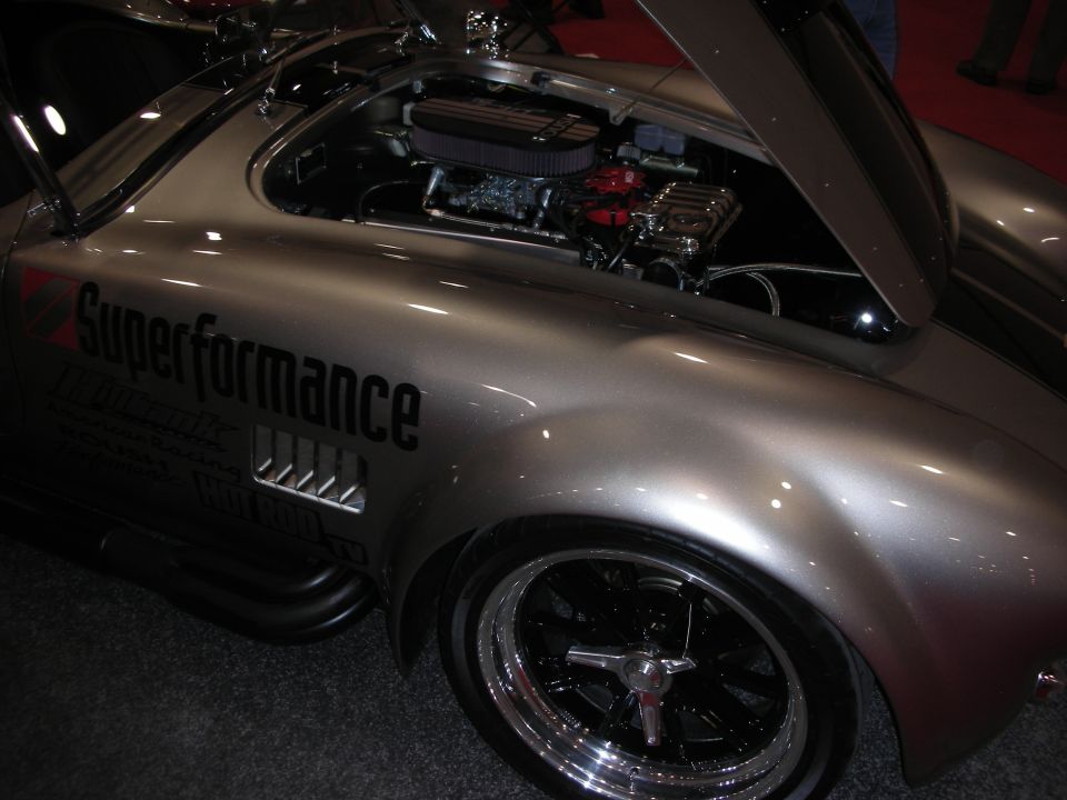 Silver Superformance Cobra-style roadster with open hood and chrome five-spoke wheel