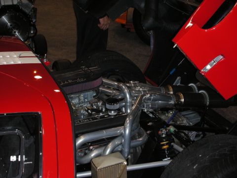 1998 Ford Crown Victoria - Engine compartment of a red car showing a finned air cleaner, chrome exhaust headers and coilover suspension.