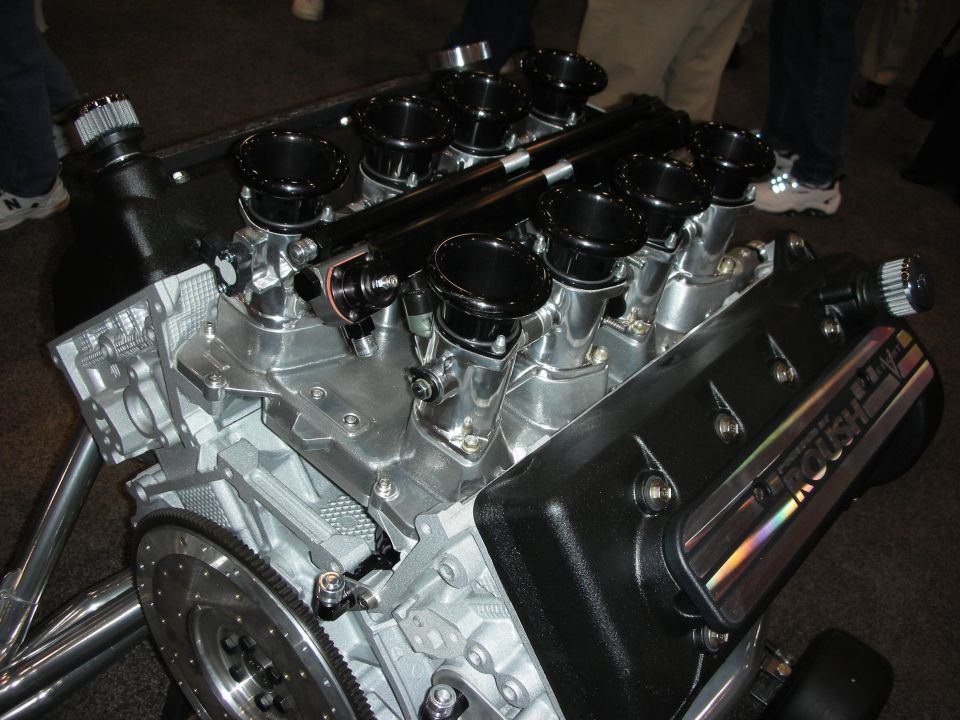 Roush V8 crate engine on a stand with black velocity-stack intakes and flywheel
