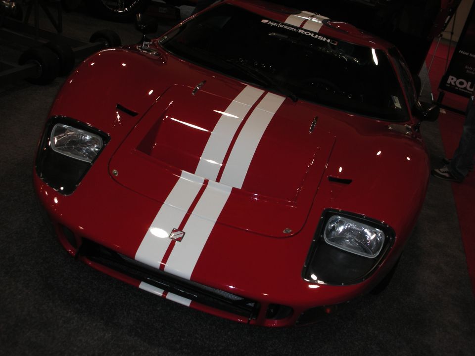 Front of a red mid-engine sports car with twin white racing stripes on the hood