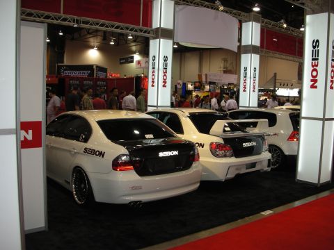 1998 Ford Crown Victoria - Seibon trade-show booth showing rear ends of white and black cars fitted with carbon-fiber trunks and spoilers.