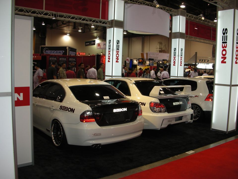 Seibon booth with rear views of white and black cars with carbon trunks and spoilers