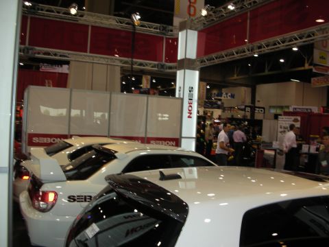 1998 Ford Crown Victoria - White tuner cars with carbon parts displayed at the Seibon booth under truss lighting on a convention floor.
