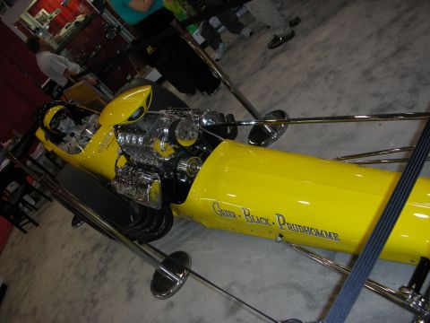 1998 Ford Crown Victoria - Yellow long-nose dragster topped with a chrome supercharged engine, viewed from the front at an angle.