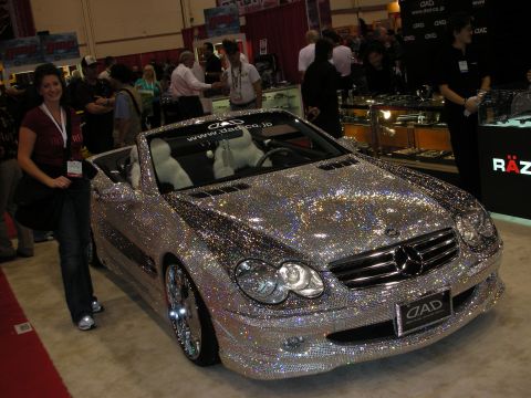 1998 Ford Crown Victoria - crystal-encrusted Mercedes-Benz convertible on a show stand, with a woman posing beside it at the DAD booth.