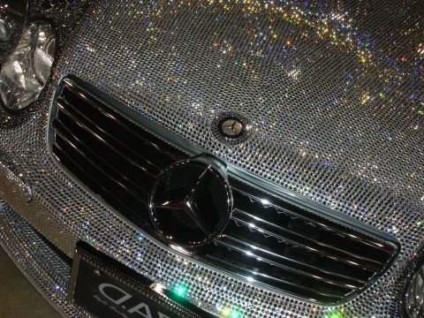 1998 Ford Crown Victoria - Close-up of the chrome grille and three-pointed-star emblem of a Mercedes-Benz coated in sparkling crystals.