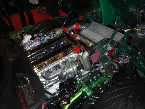 1998 Ford Crown Victoria - Engine bay of a green custom car featuring gold valve covers, a top-mount intercooler and turbo piping.