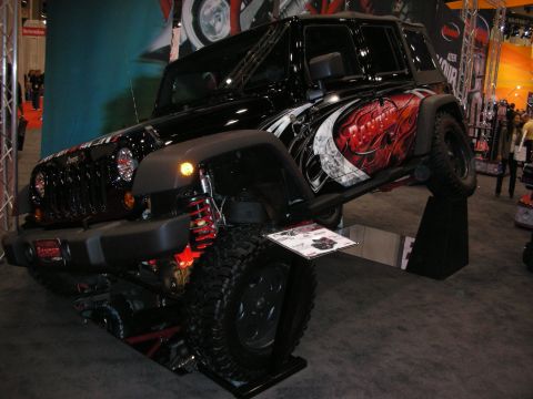 1998 Ford Crown Victoria - black four-door Jeep Wrangler with red and white graphics sits raised on a rotating display stand at an indoor show.