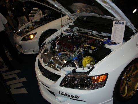 1998 Ford Crown Victoria - open engine bay of a white car shows a polished GReddy turbocharged engine beside a posted tune-up spec sheet at a show.