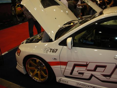 1998 Ford Crown Victoria - white show car with its hood up displays gold multi-spoke wheels and side graphics reading GReddy, T67 and Grex.
