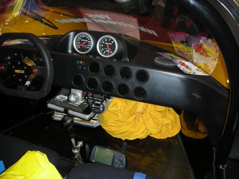 1998 Ford Crown Victoria - stripped race-car cockpit shows a Sparco steering wheel, twin gauges, switch panel and a folded yellow parachute pack.