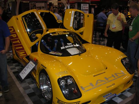 1998 Ford Crown Victoria - bright yellow mid-engine supercar with upward-opening doors and Hahn graphics sits on display at an indoor automotive show.