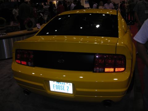 1998 Ford Crown Victoria - rear of a yellow Ford Mustang coupe shows blacked-out trim and a Texas license plate reading FOOSE 2 at a show.