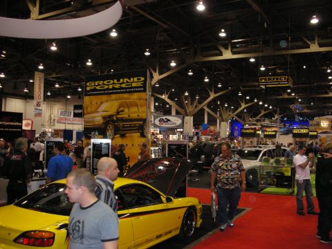 1998 Ford Crown Victoria - Crowds move past yellow and black show cars under a Ground Force suspension banner in a large convention hall.