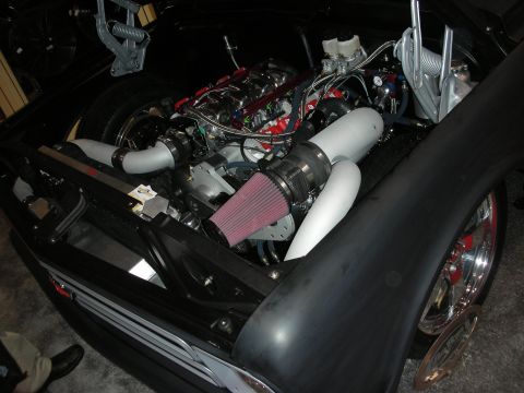 1998 Ford Crown Victoria - supercharged engine with a red cone air filter and silver piping fills the bay of a matte-black car with chrome wheels.