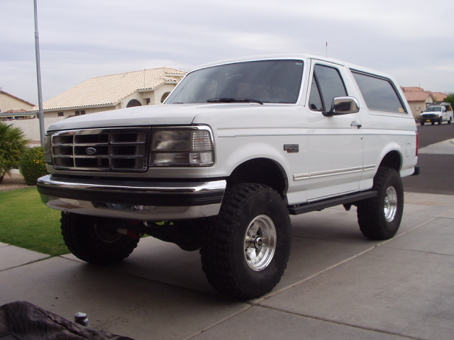White lifted Ford Bronco SUV on big tires parked in a driveway, front 3/4 view