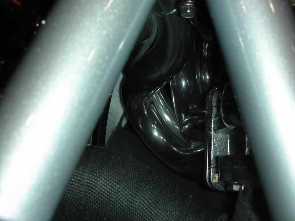 Close-up of glossy black engine bay component framed by a silver tubular roll cage bar