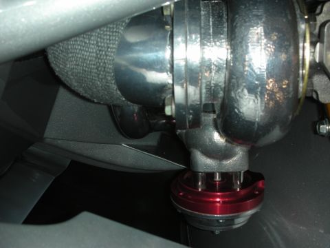1998 Ford Crown Victoria - turbocharger with a polished metal compressor housing sits beside a red anodized wastegate inside an engine bay.
