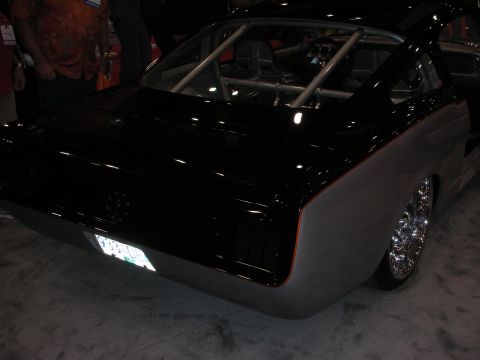 1998 Ford Crown Victoria - black custom fastback muscle car with chrome wheels and a visible roll cage sits on display at an indoor event.